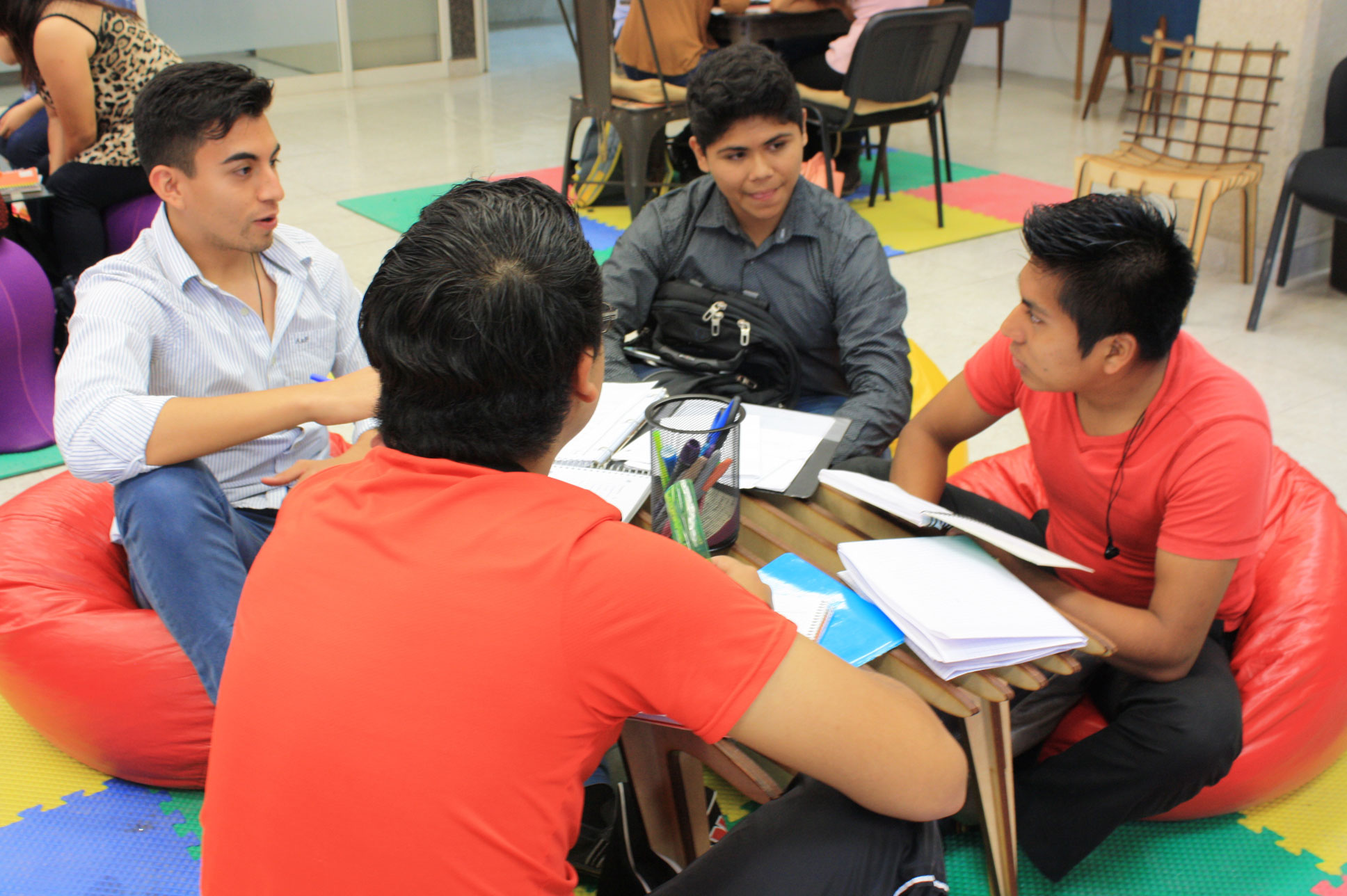 La imagen muestra a varios estudiantes trabajando juntos en el aula POETA.
